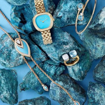 Photographie de joaillerie sur fond turquoise mettant en scène montre et bijoux sertis de diamants et pierres bleu.
