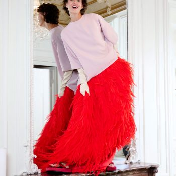 Photographie de mode éditoriale par le photographe Alex Fadel pour Elle Arabia. Mannequin Alyosha K en jupe de plumes rouge vif et haut lilas Full Look Balenciaga , posant sur une cheminée ancienne à la Maison Delano Paris. Stylisme Farouk Chekoufi.